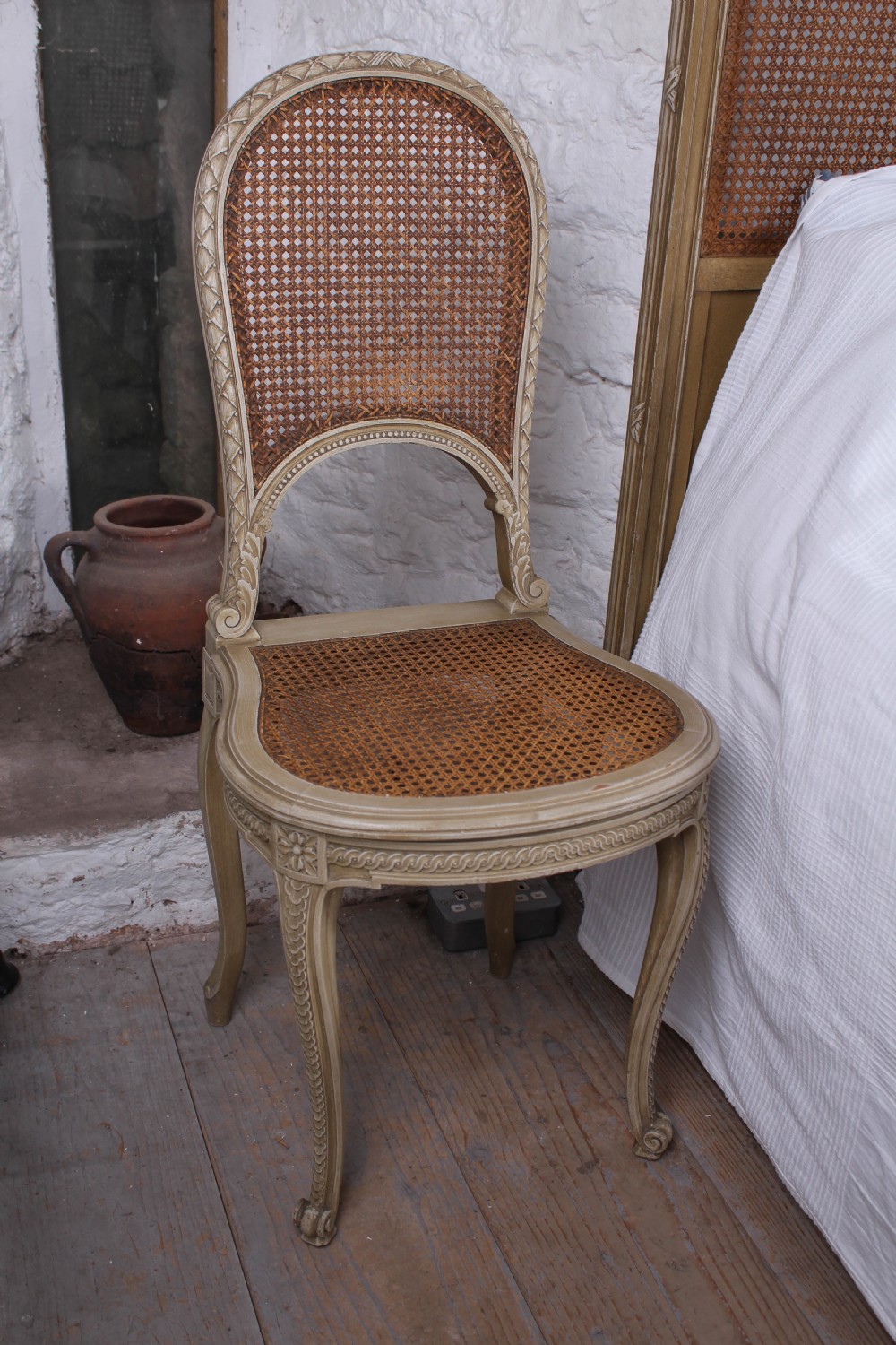 A French Louis XVI style super king bedstead featuring woven rattan cane panels, carved floral swags, and matching caned side chairs in a painted distressed finish. View XII