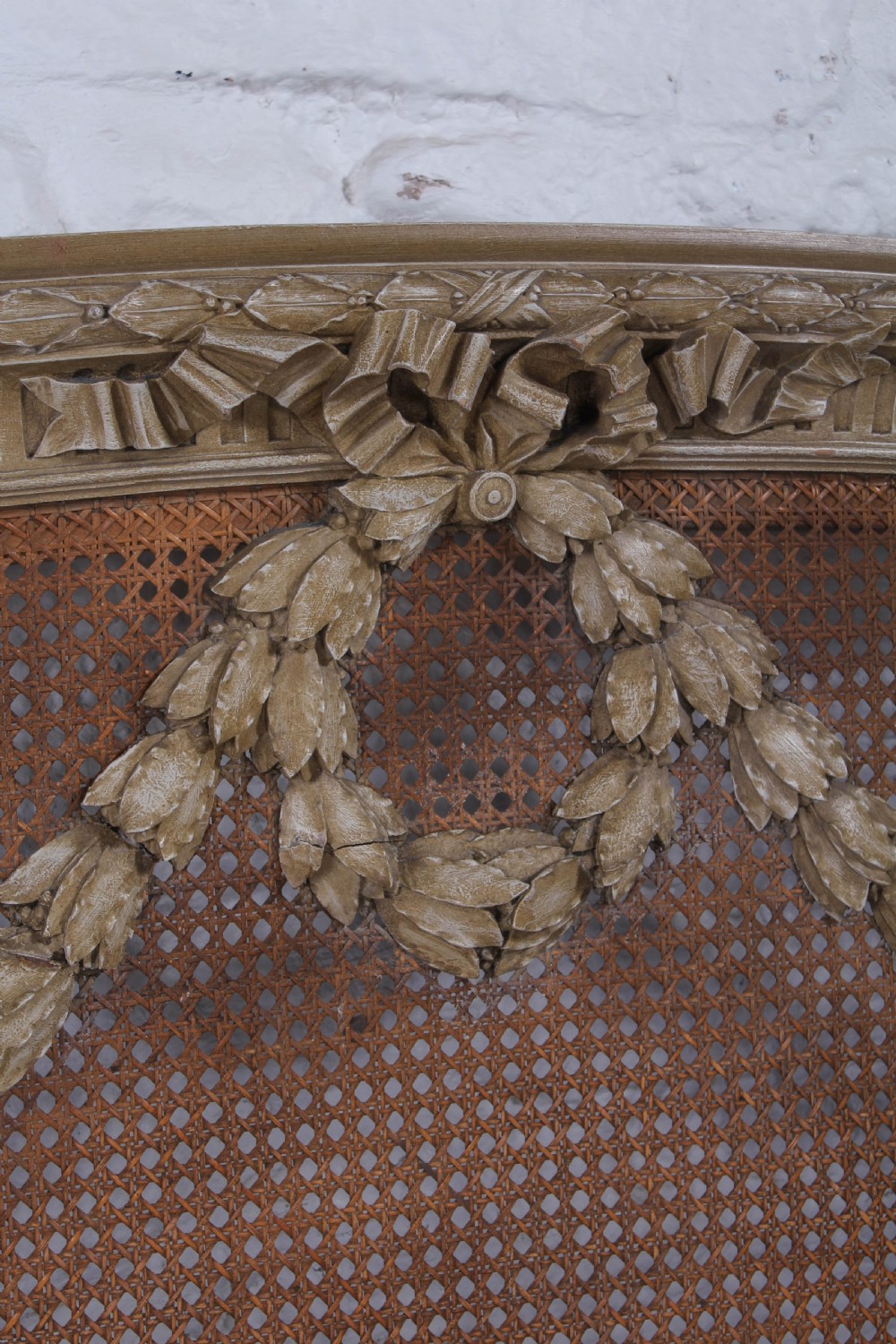 A French Louis XVI style super king bedstead featuring woven rattan cane panels, carved floral swags, and matching caned side chairs in a painted distressed finish. View XV