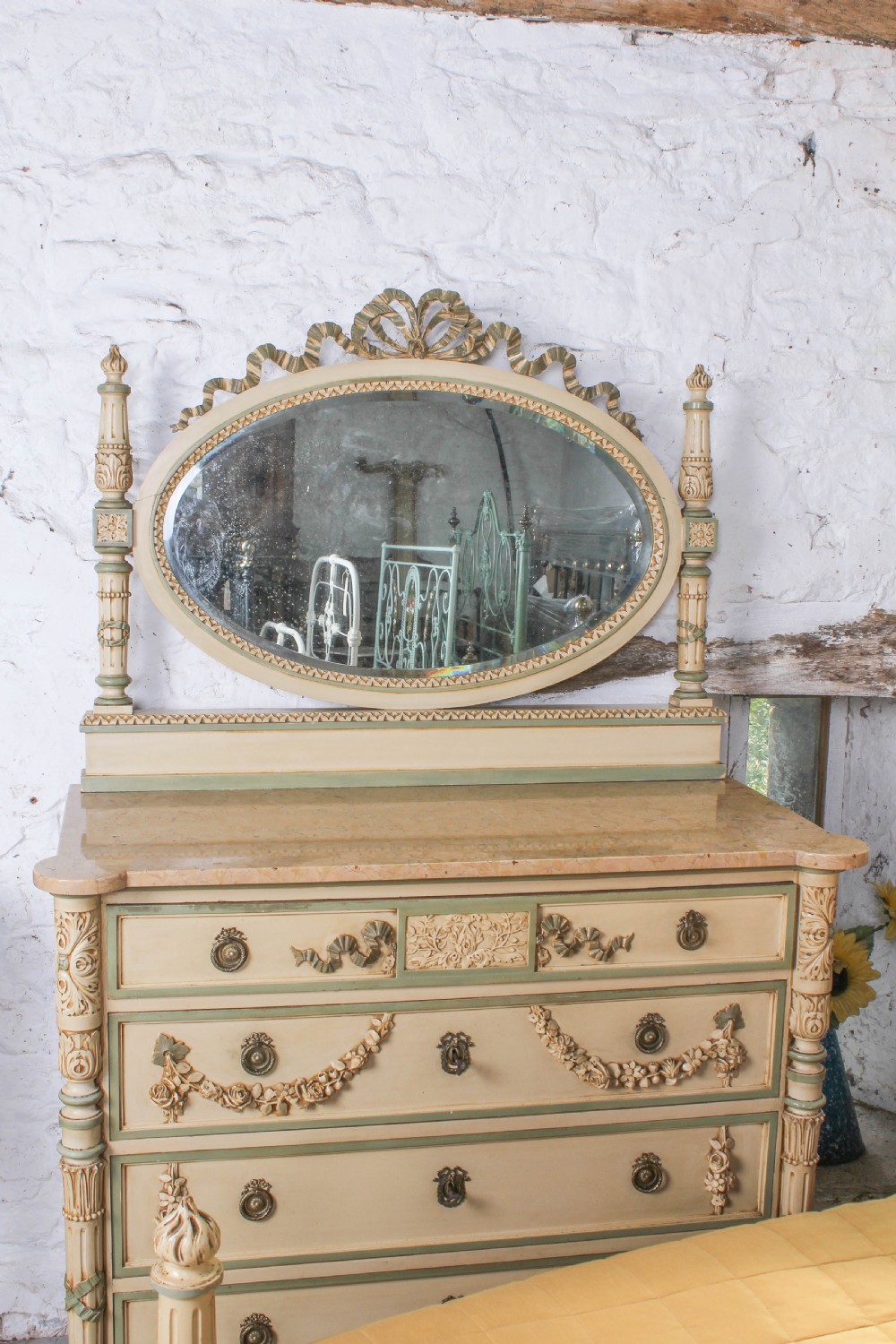 A cream and green painted super king size bedroom set featuring a detailed caned headboard, carved garlands, two matching bedside tables, and a chest of drawers with an oval mirror. View V
