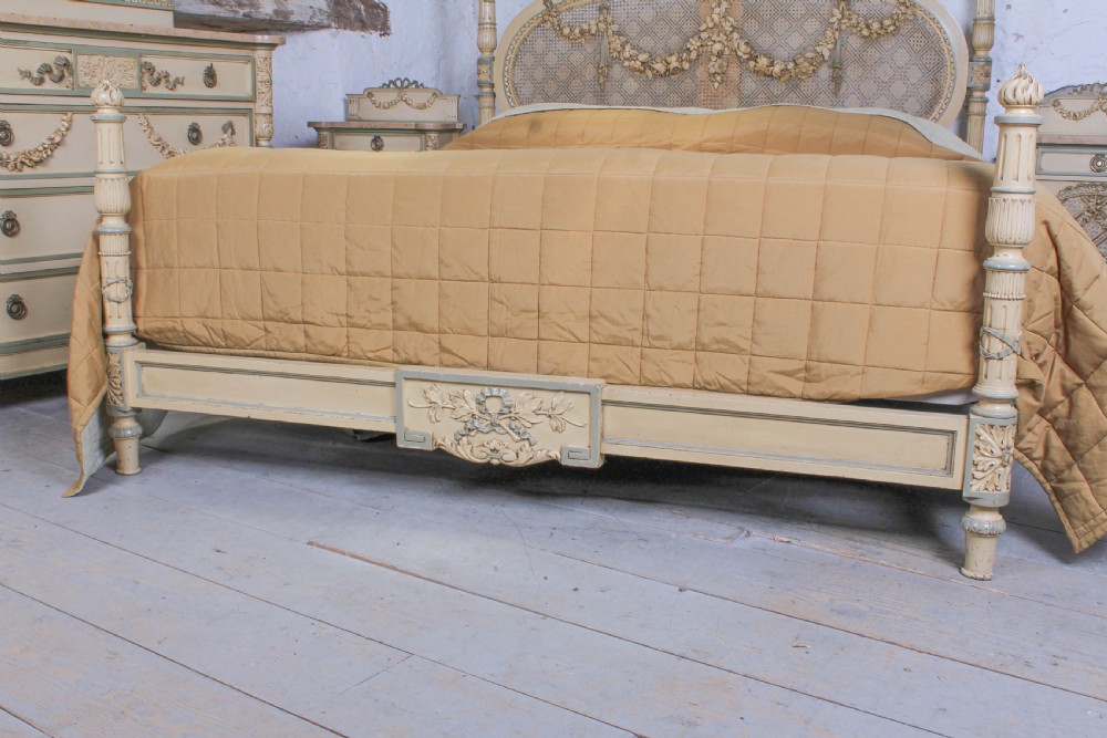 A cream and green painted super king size bedroom set featuring a detailed caned headboard, carved garlands, two matching bedside tables, and a chest of drawers with an oval mirror. View VI