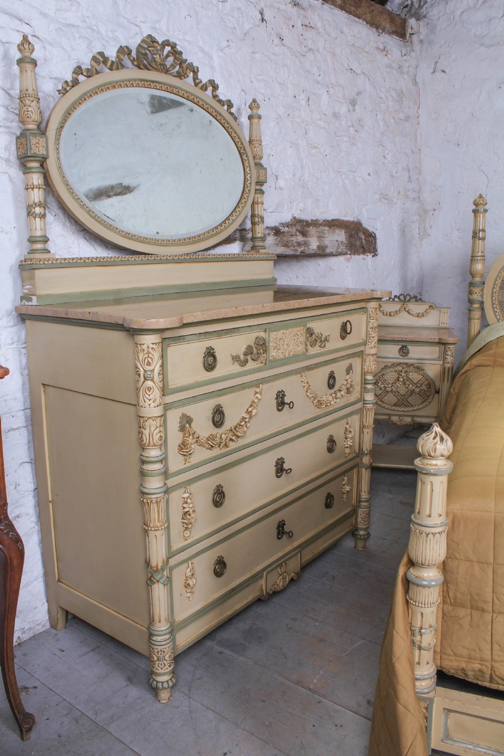 A cream and green painted super king size bedroom set featuring a detailed caned headboard, carved garlands, two matching bedside tables, and a chest of drawers with an oval mirror. View VII