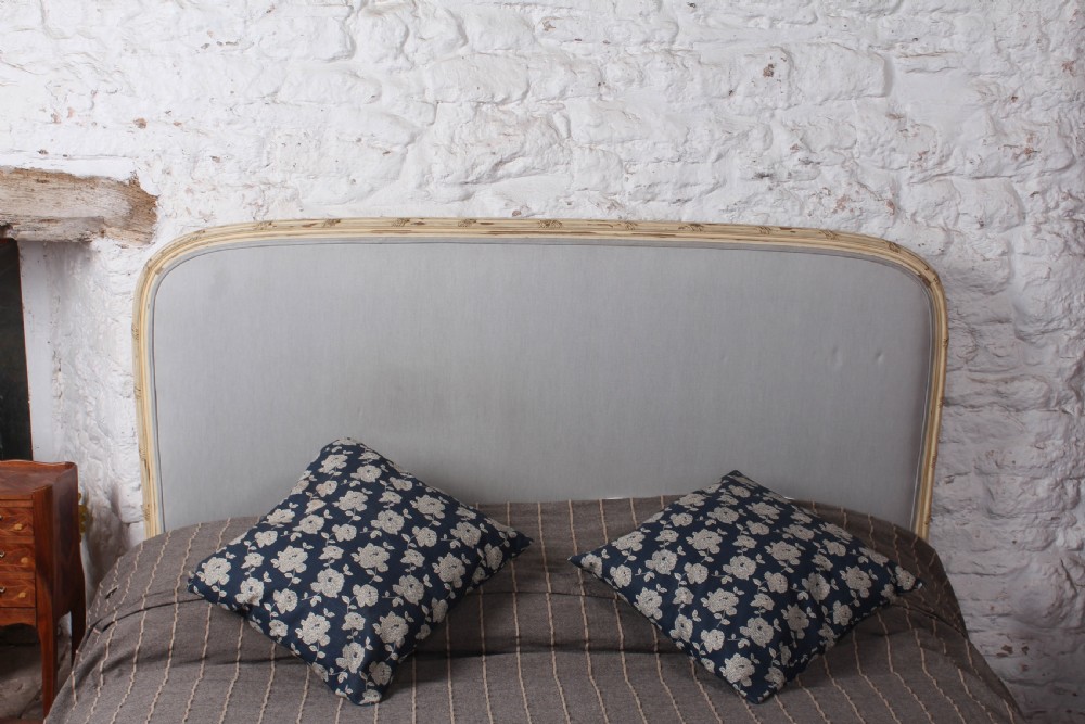 An antique French king-size bed featuring a cream painted carved wooden frame and light grey upholstered panels on the headboard and footboard. View II