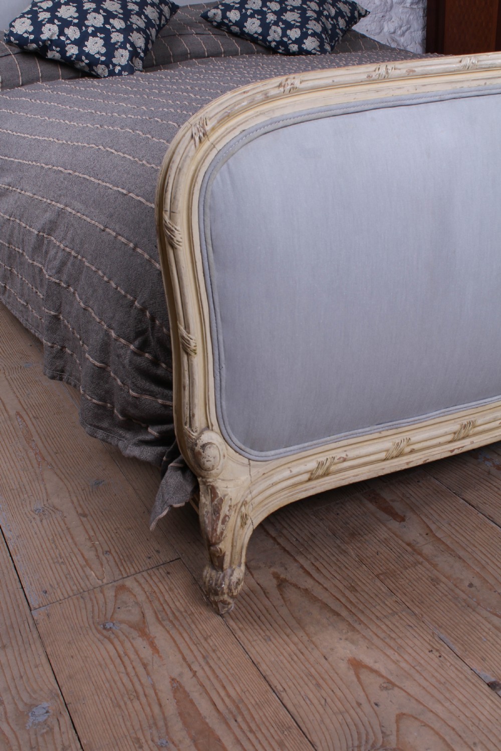 An antique French king-size bed featuring a cream painted carved wooden frame and light grey upholstered panels on the headboard and footboard. View V