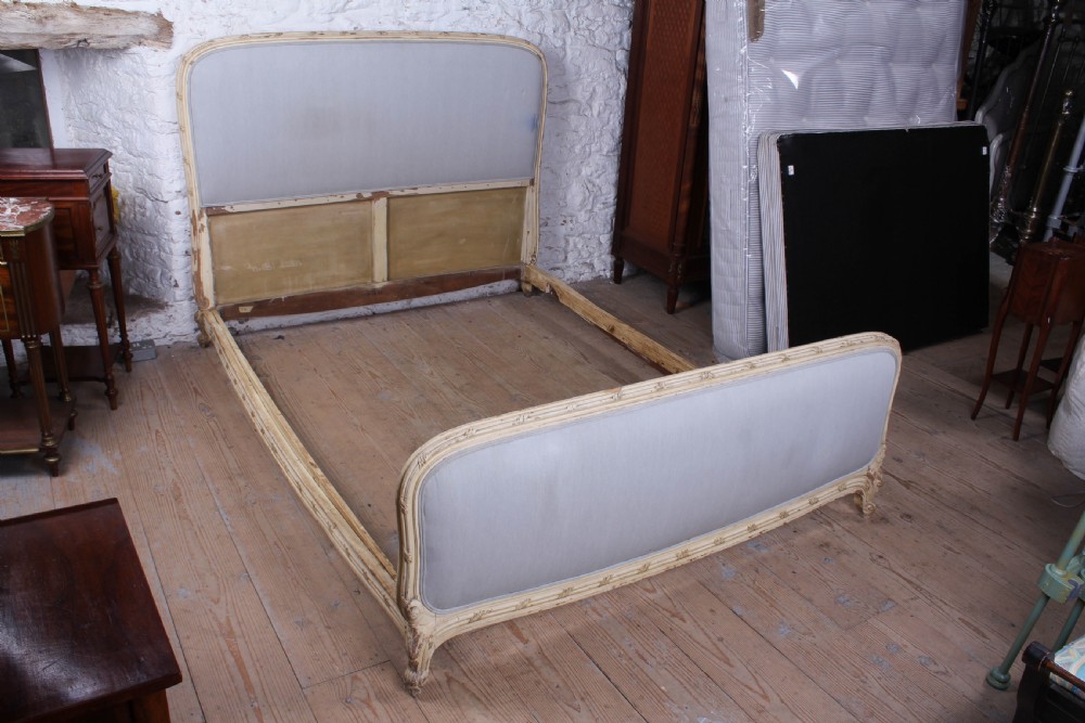 An antique French king-size bed featuring a cream painted carved wooden frame and light grey upholstered panels on the headboard and footboard. View VI