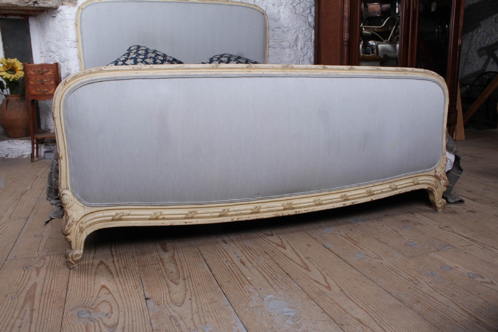 An antique French king-size bed featuring a cream painted carved wooden frame and light grey upholstered panels on the headboard and footboard. View VII