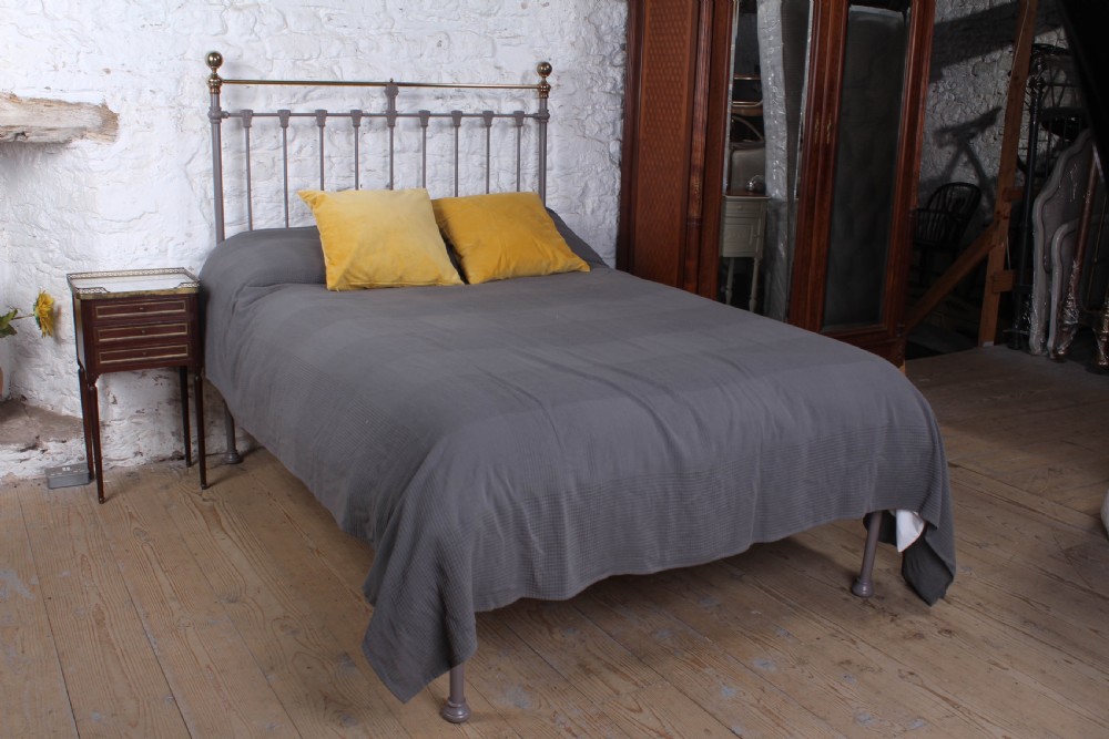 A Victorian double bed frame featuring a grey painted cast iron headboard with vertical spindles, a polished brass top rail, corner finials, and no footboard.