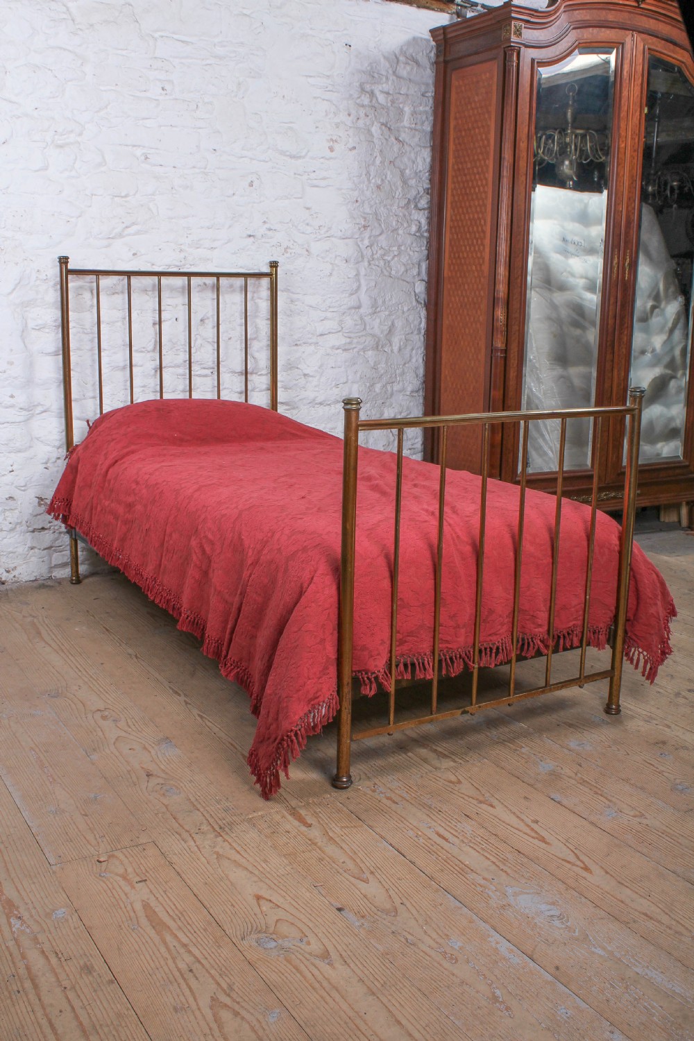 An antique single brass bedstead featuring vertical tubular spindles and a matching headboard and footboard with brass finials.