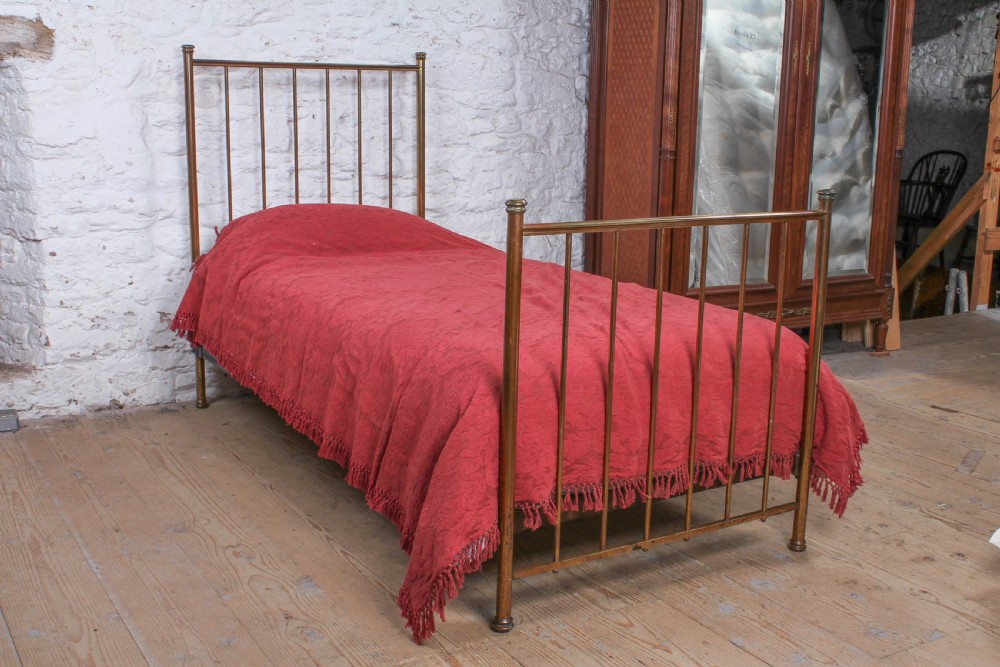 An antique single brass bedstead featuring vertical tubular spindles and a matching headboard and footboard with brass finials. View II
