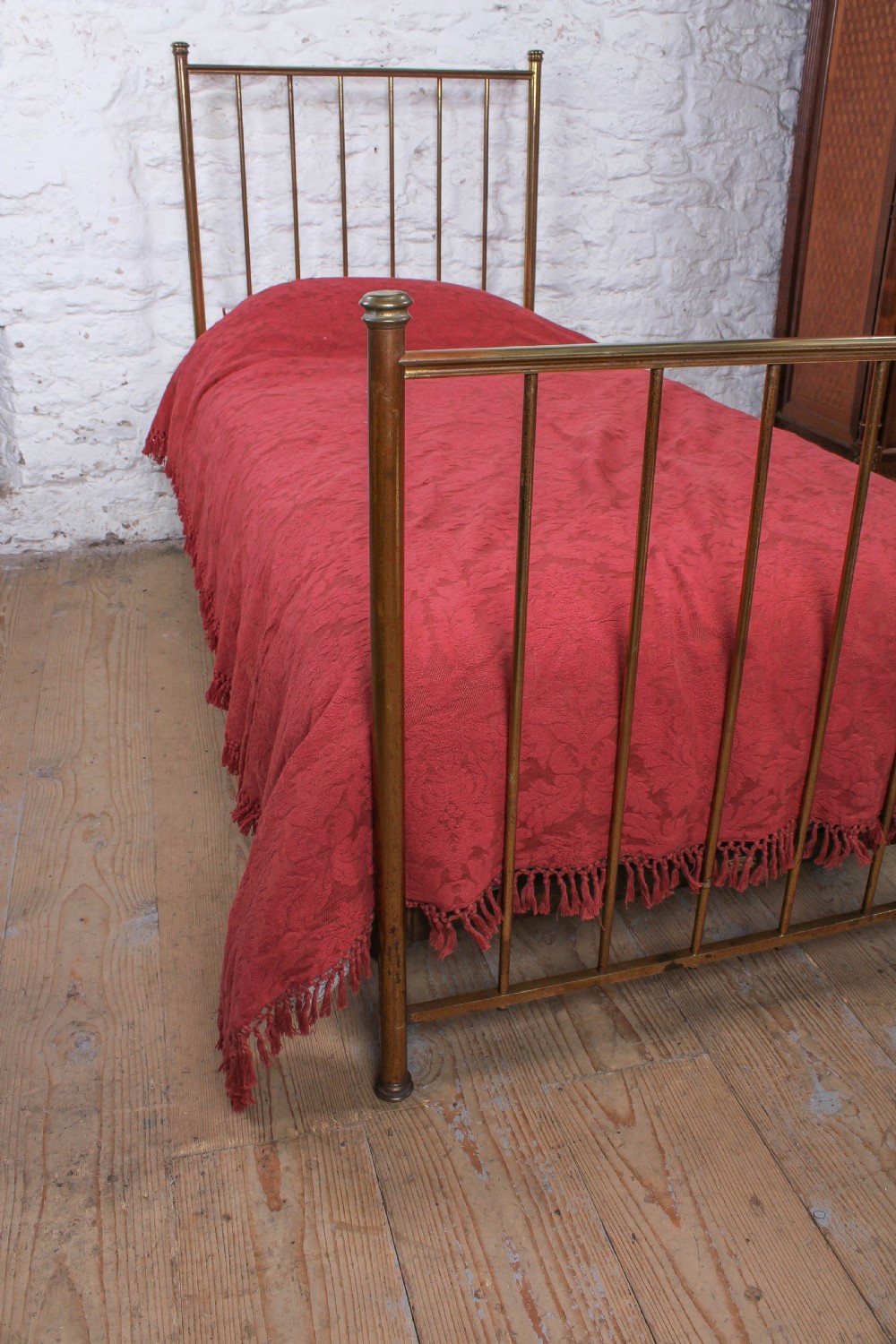An antique single brass bedstead featuring vertical tubular spindles and a matching headboard and footboard with brass finials. View V