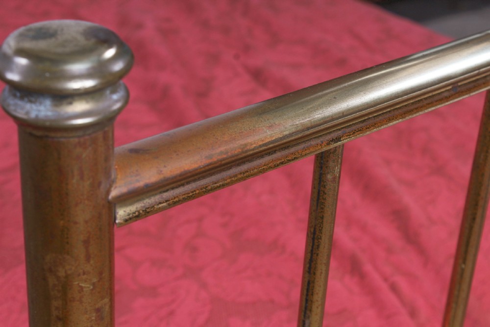 An antique single brass bedstead featuring vertical tubular spindles and a matching headboard and footboard with brass finials. View VI