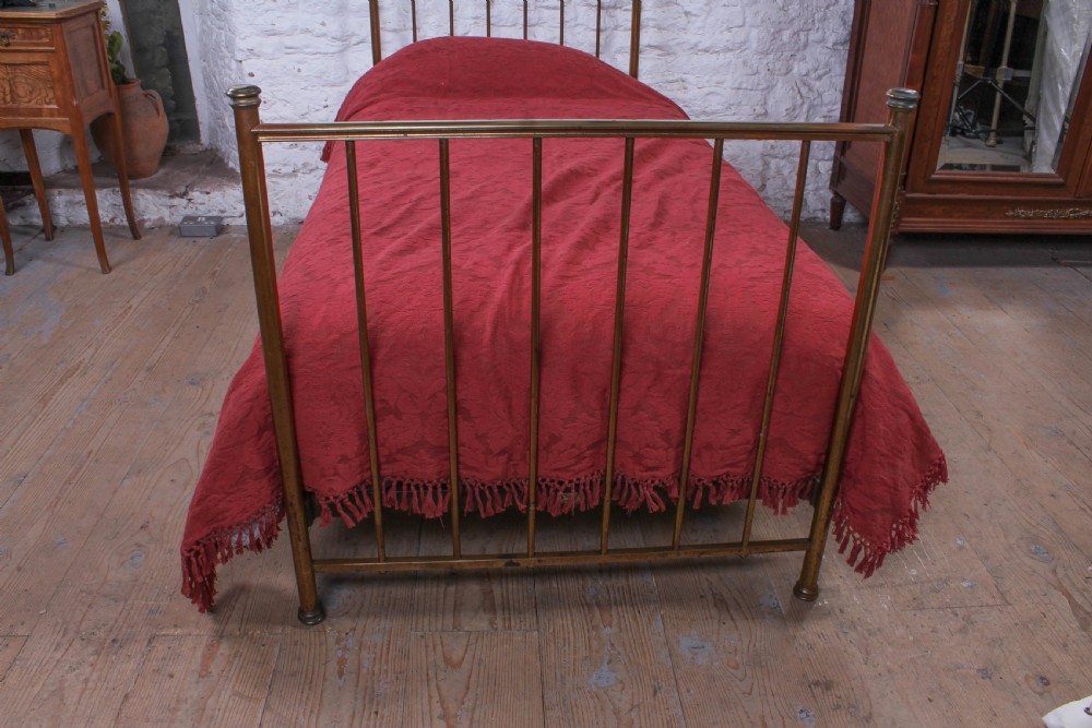 An antique single brass bedstead featuring vertical tubular spindles and a matching headboard and footboard with brass finials. View VIII