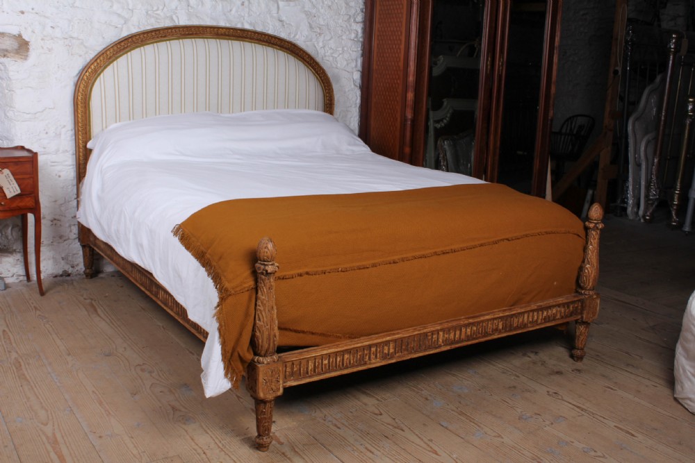 A Louis XVI style king size bed frame featuring a carved timber border, a striped upholstered arched headboard, and low carved corner posts.