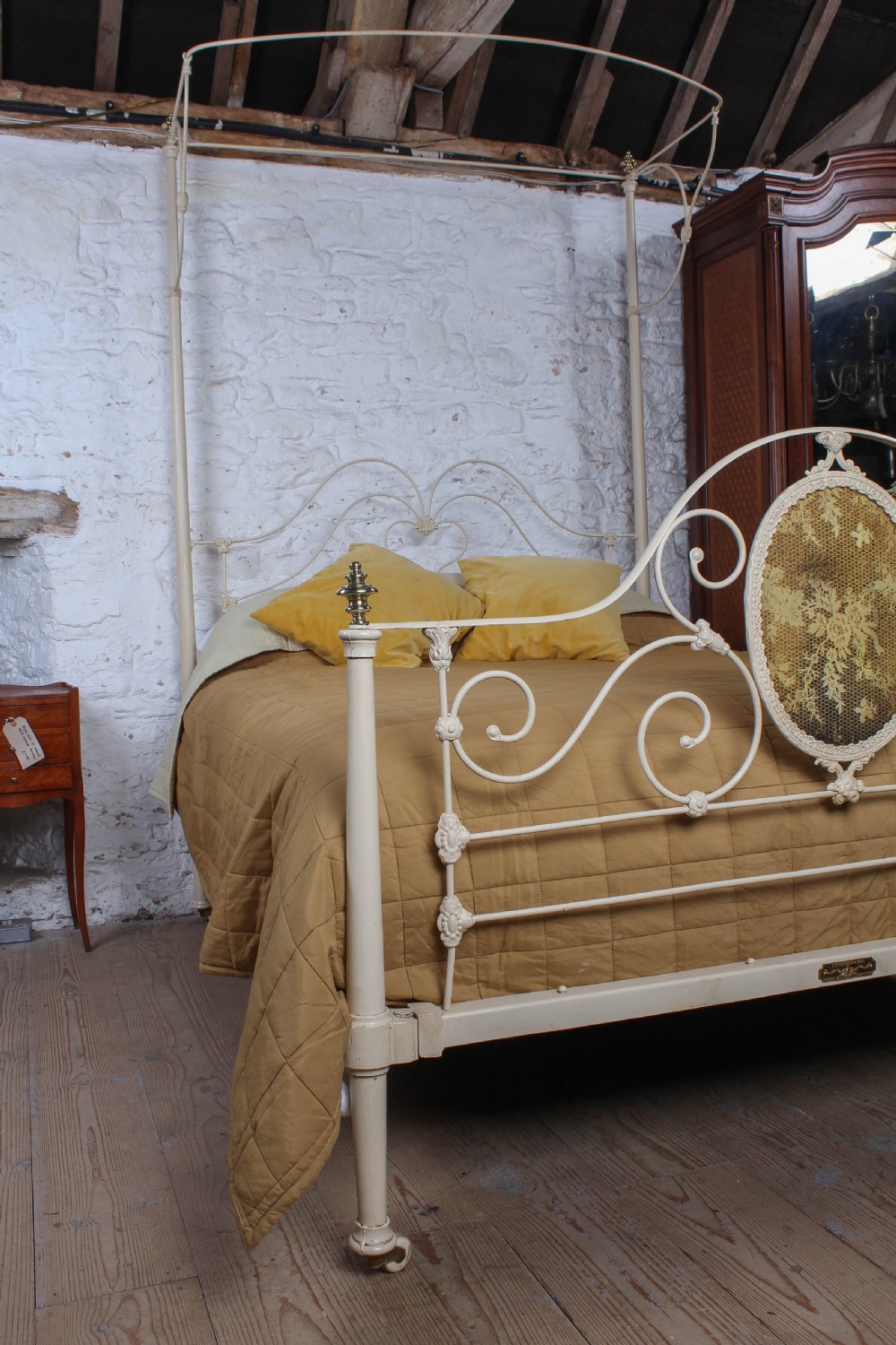 A cream painted wrought iron king size half tester bed frame featuring an ornate scrollwork footboard with a central oval medallion and brass finials. View VII