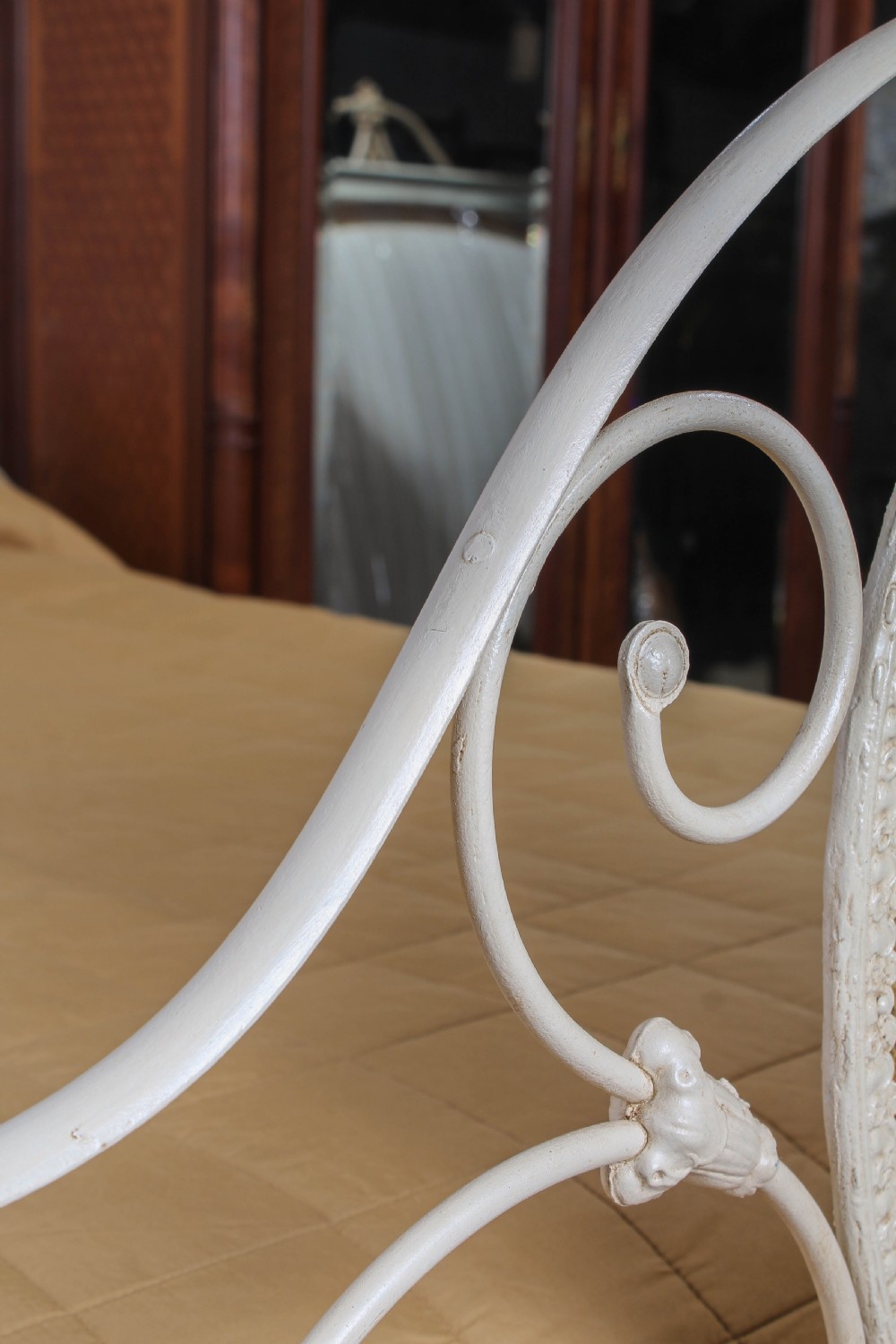 A cream painted wrought iron king size half tester bed frame featuring an ornate scrollwork footboard with a central oval medallion and brass finials. View X
