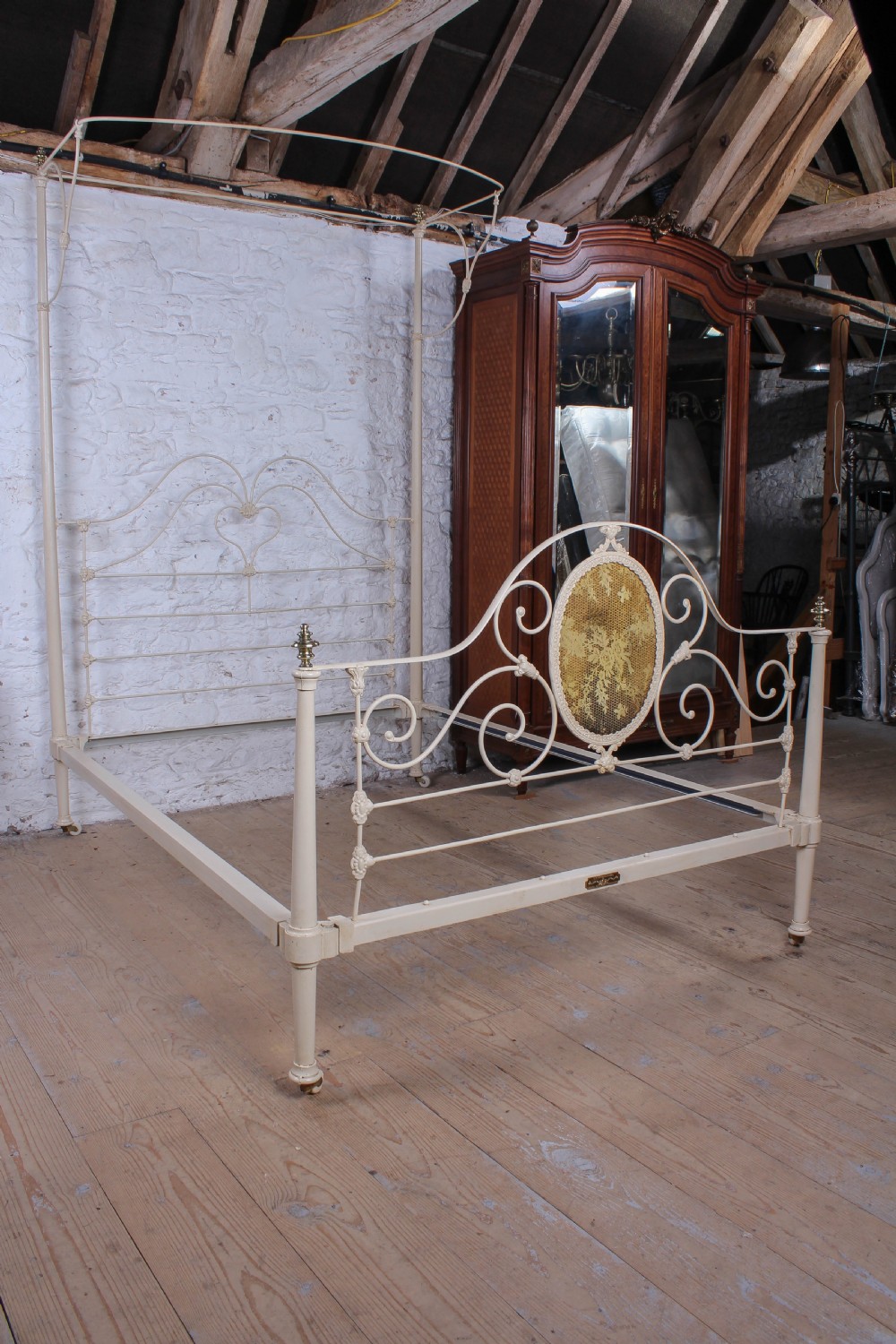 A cream painted wrought iron king size half tester bed frame featuring an ornate scrollwork footboard with a central oval medallion and brass finials. View XI
