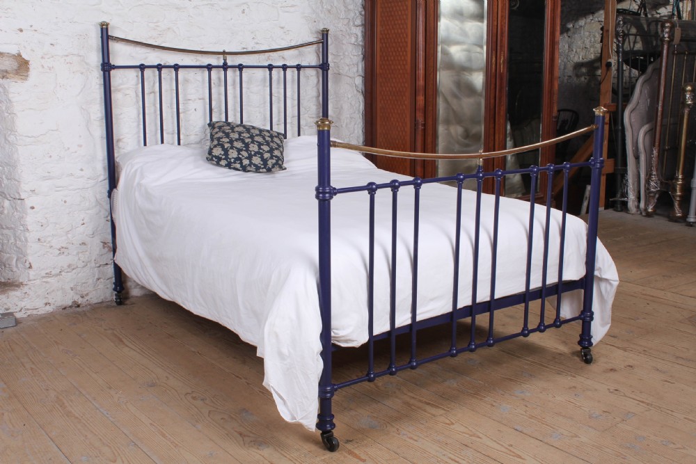 A Victorian metal double bedstead featuring a dark blue painted frame, vertical spindles, dipped brass top rails, and brass corner finials.