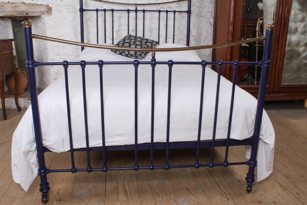 A Victorian metal double bedstead featuring a dark blue painted frame, vertical spindles, dipped brass top rails, and brass corner finials. View V