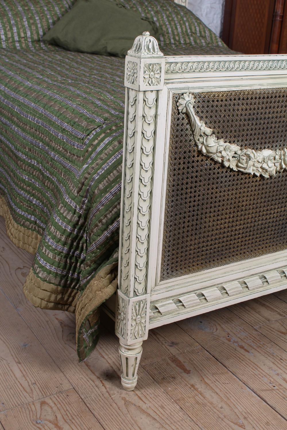 A painted Louis XVI style double bed frame featuring carved floral garlands, fluted corner posts, and woven cane panels in the headboard and footboard. View VI