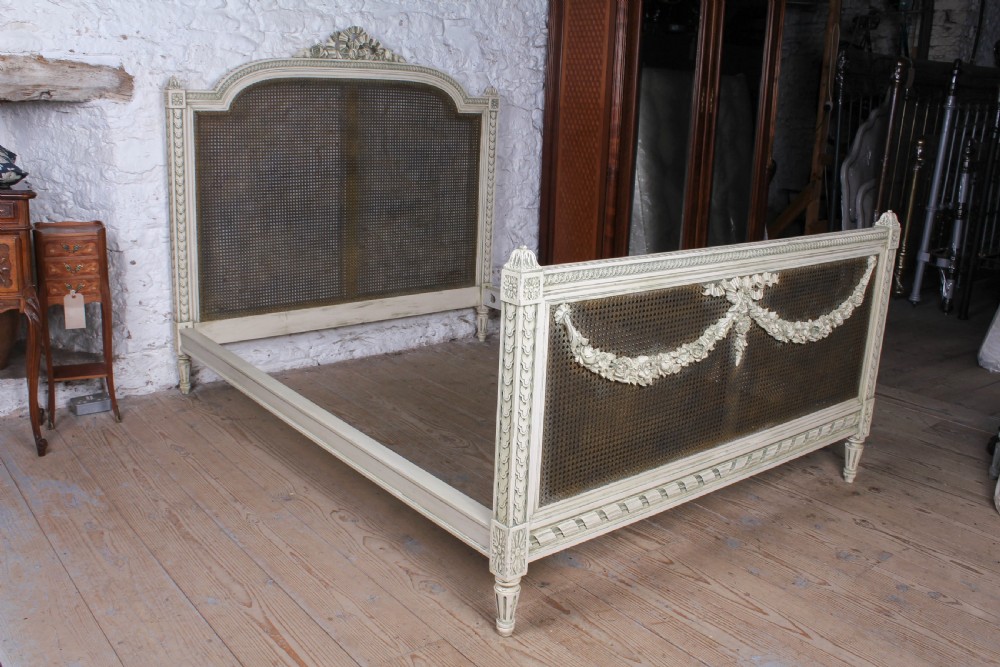 A painted Louis XVI style double bed frame featuring carved floral garlands, fluted corner posts, and woven cane panels in the headboard and footboard. View VIII