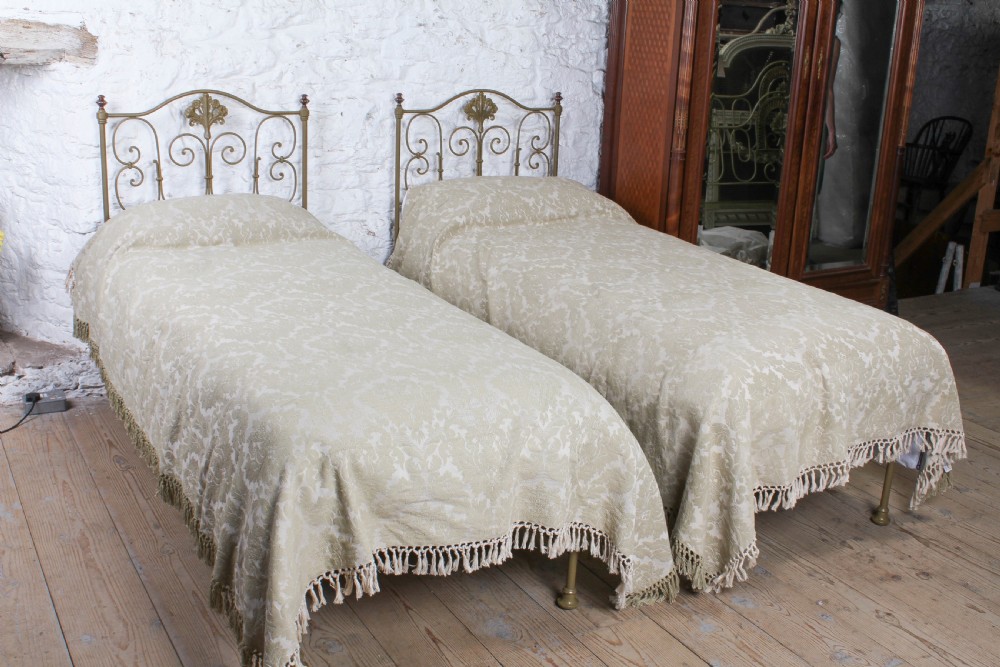 A pair of antique Portuguese small single metal beds featuring arched headboards with ornate metal scrollwork and central shell motifs.