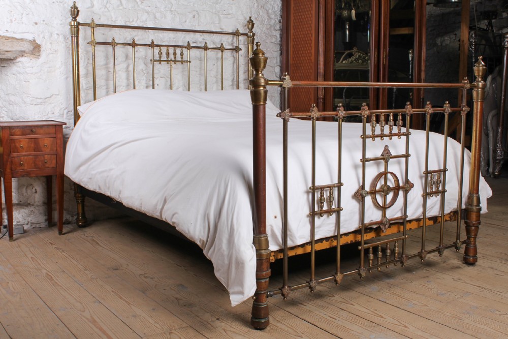 A Victorian king-size brass bed frame featuring detailed vertical spindles, geometric central motifs on the footboard, and turned corner posts with finials.