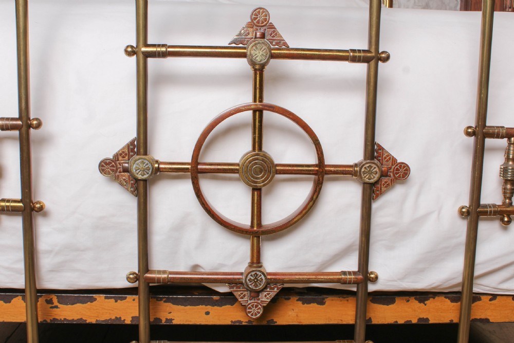 A Victorian king-size brass bed frame featuring detailed vertical spindles, geometric central motifs on the footboard, and turned corner posts with finials. View VII