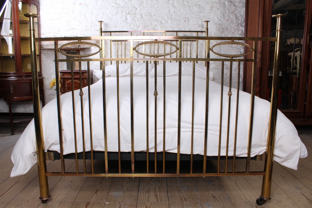 An antique brass king-size bed frame featuring vertical spindles, decorative oval motifs, and four tapered posts on castors. View II
