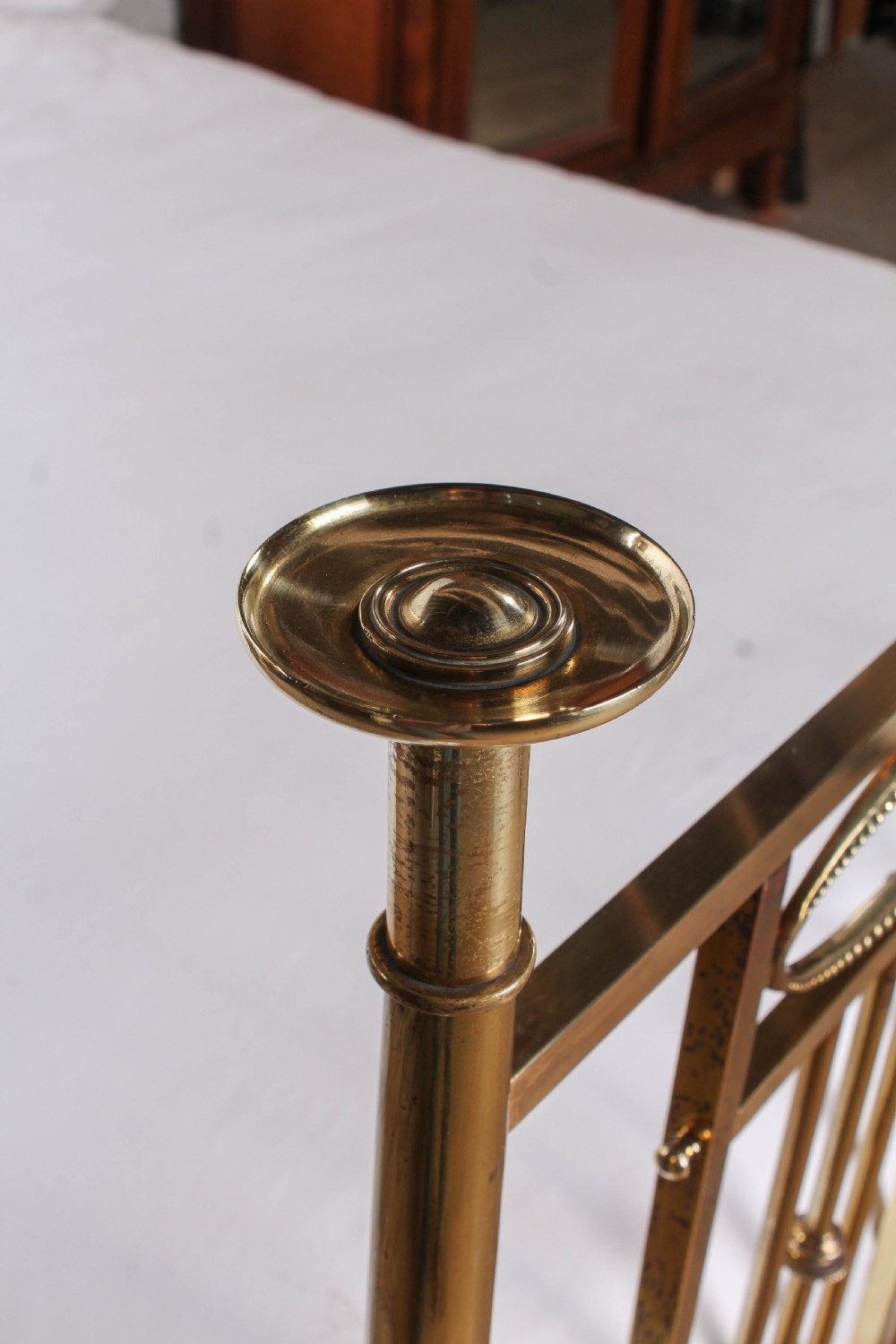 An antique brass king-size bed frame featuring vertical spindles, decorative oval motifs, and four tapered posts on castors. View VI