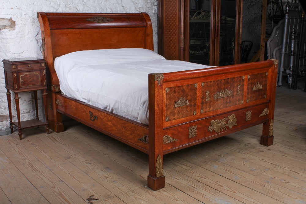 An Empire style mahogany double bedstead featuring rolled headboard profiles, parquetry panelwork, and decorative gilt-bronze mounts.