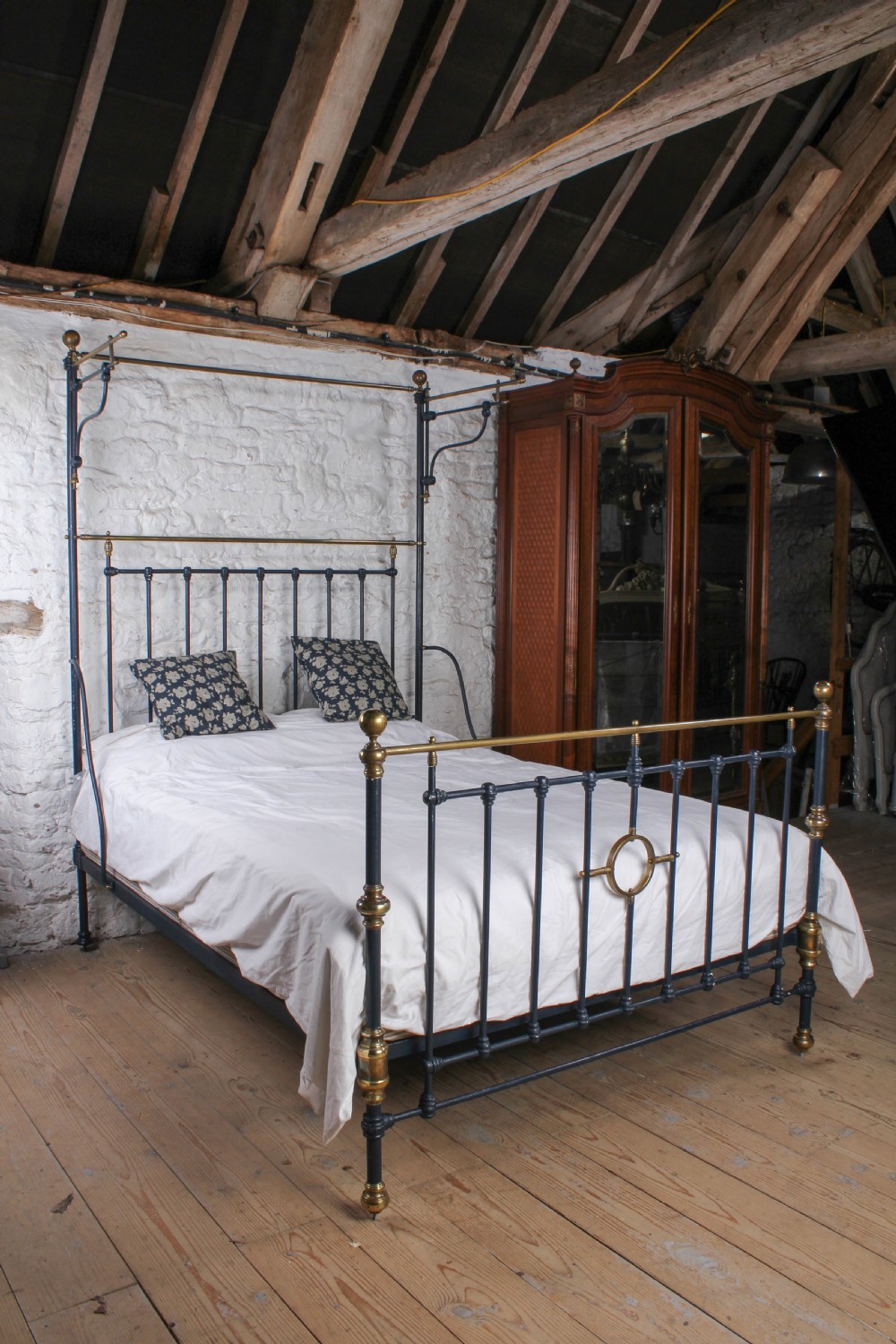 A Victorian black iron and brass king size half tester bed featuring vertical spindles and turned brass finials.