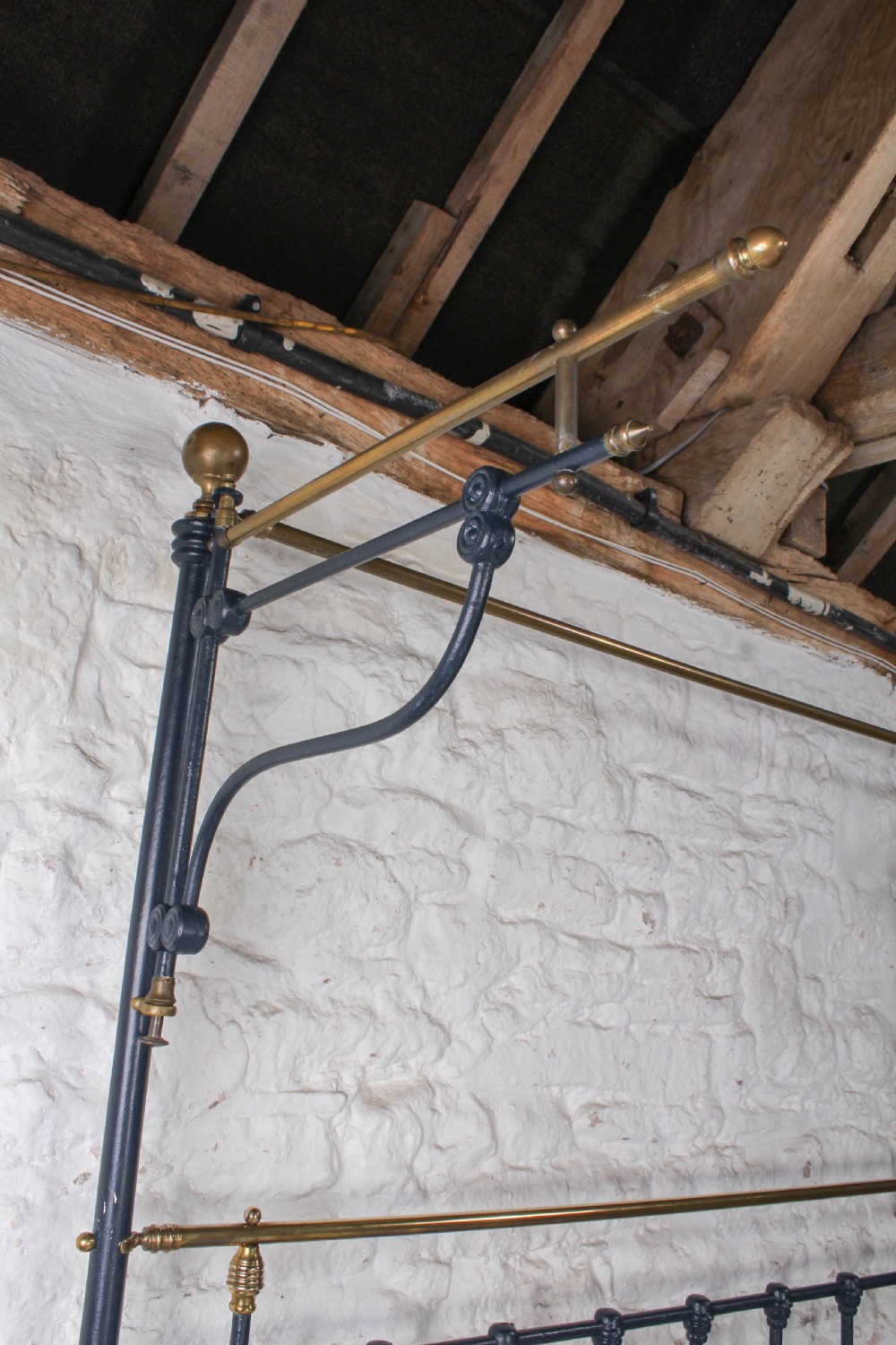 A Victorian black iron and brass king size half tester bed featuring vertical spindles and turned brass finials. View V
