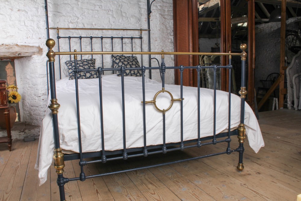 A Victorian black iron and brass king size half tester bed featuring vertical spindles and turned brass finials. View VI