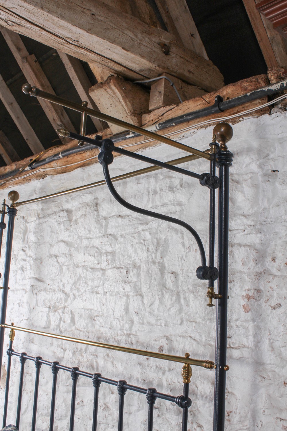 A Victorian black iron and brass king size half tester bed featuring vertical spindles and turned brass finials. View VII