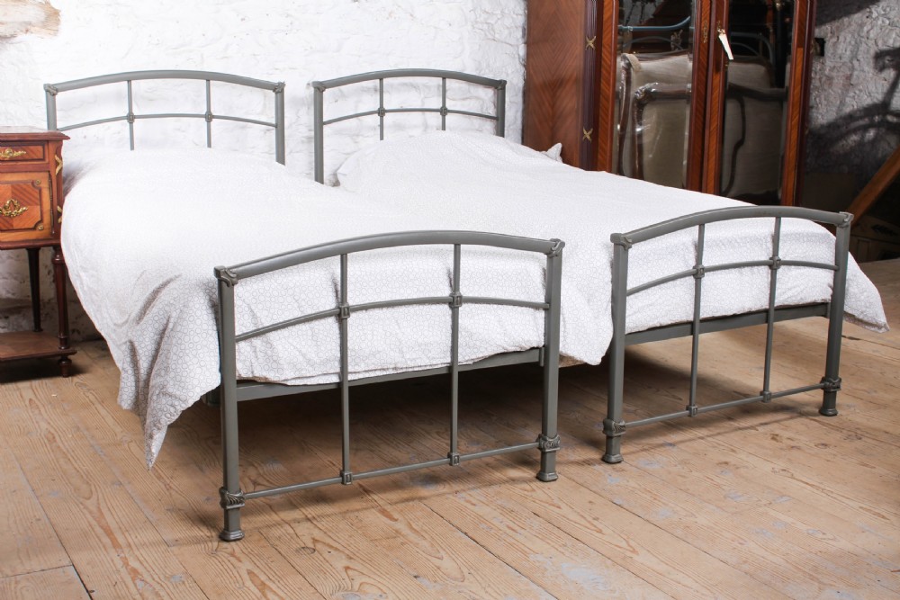 A pair of grey painted Victorian iron single beds with simple arched headboards and footboards.