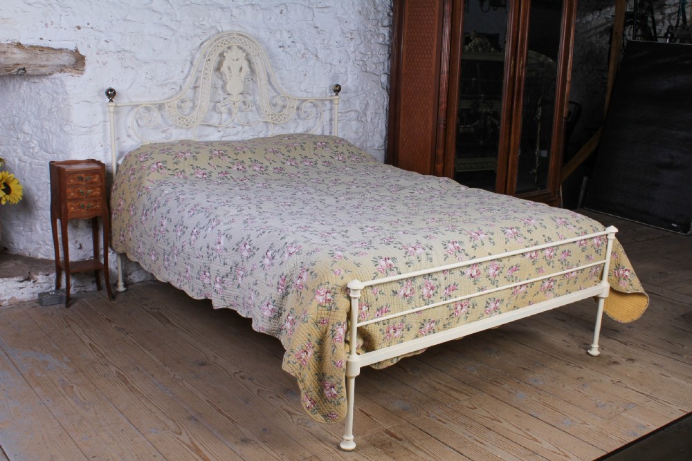 A king-size cream painted forged iron bedstead featuring an arched scrollwork headboard with a central decorative crest and a low footboard.
