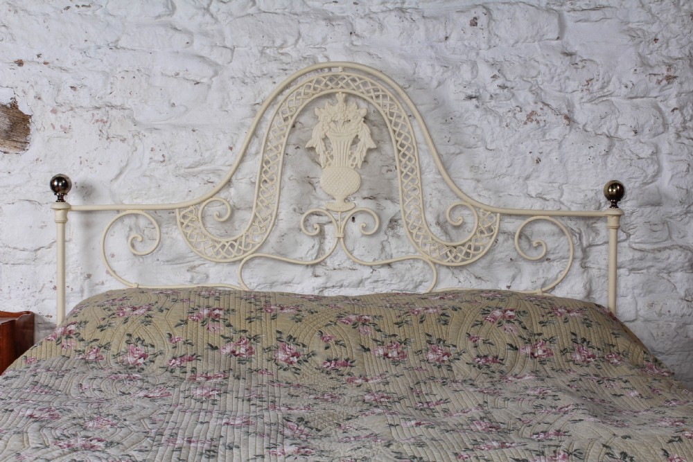 A king-size cream painted forged iron bedstead featuring an arched scrollwork headboard with a central decorative crest and a low footboard. View III