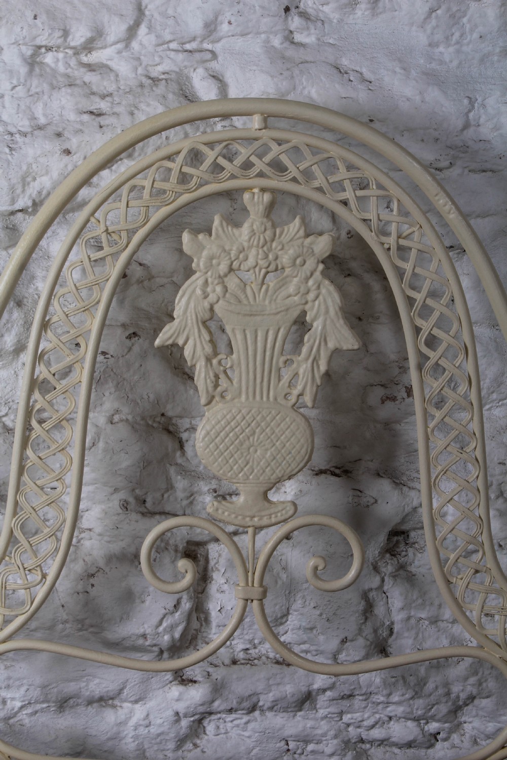 A king-size cream painted forged iron bedstead featuring an arched scrollwork headboard with a central decorative crest and a low footboard. View IV