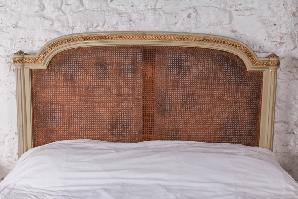 A French Louis XVI style king size bedstead featuring cream painted and gilded carved wood with natural woven cane panels on the headboard and footboard. View II
