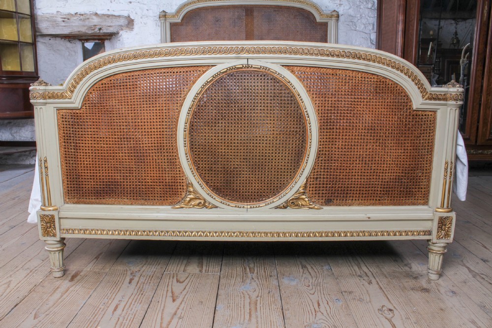 A French Louis XVI style king size bedstead featuring cream painted and gilded carved wood with natural woven cane panels on the headboard and footboard. View III