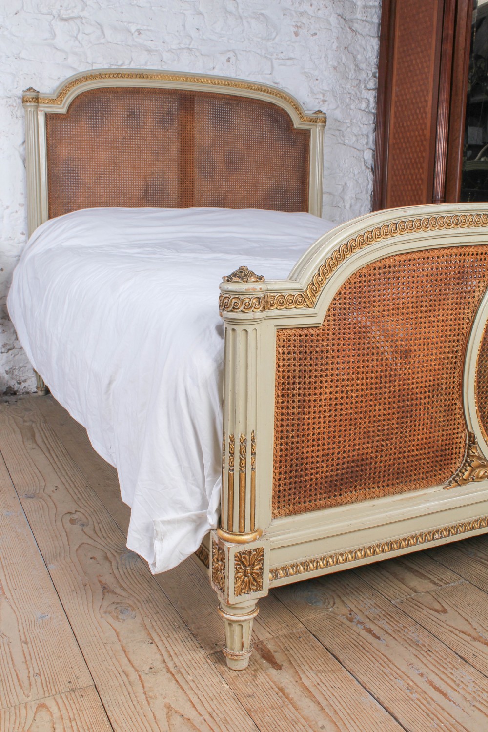 A French Louis XVI style king size bedstead featuring cream painted and gilded carved wood with natural woven cane panels on the headboard and footboard. View V