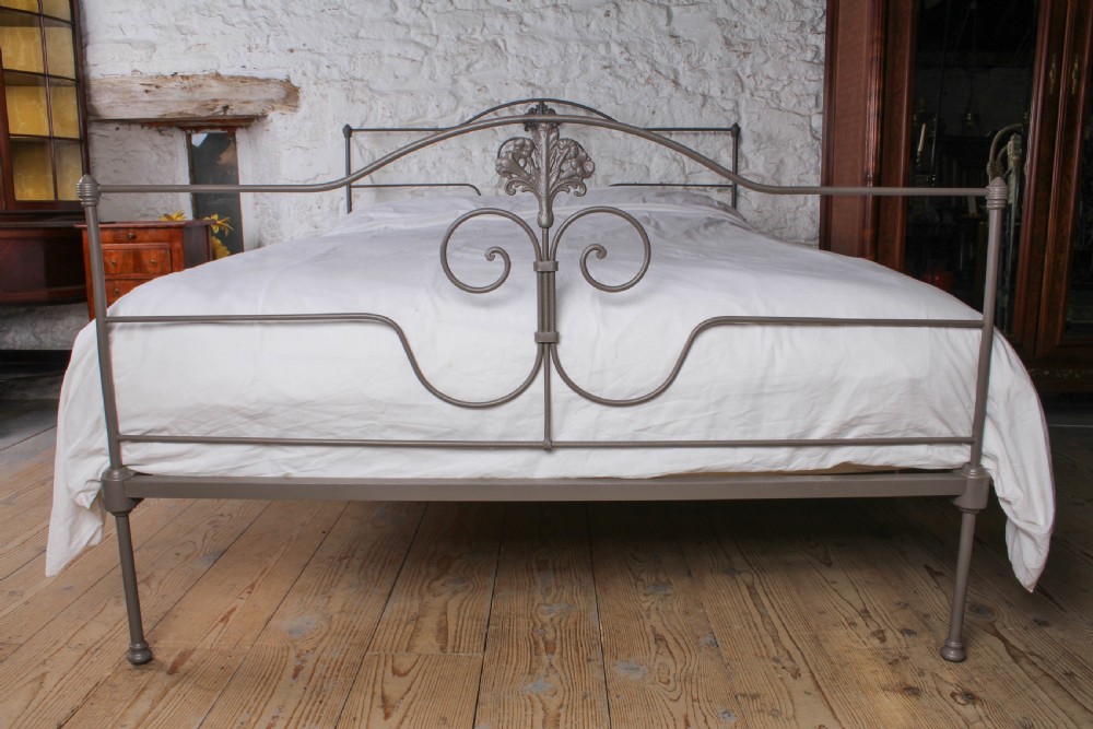 A king size Portuguese iron bed frame painted in a neutral taupe colour, featuring decorative scrollwork and a central shell motif on both the headboard and footboard. View III