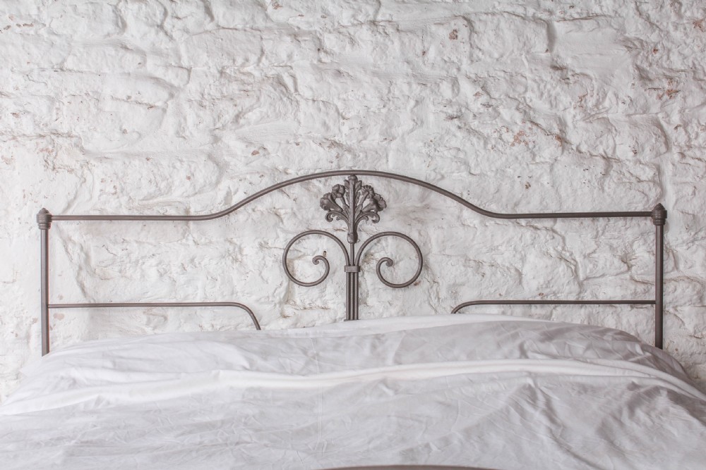 A king size Portuguese iron bed frame painted in a neutral taupe colour, featuring decorative scrollwork and a central shell motif on both the headboard and footboard. View IV