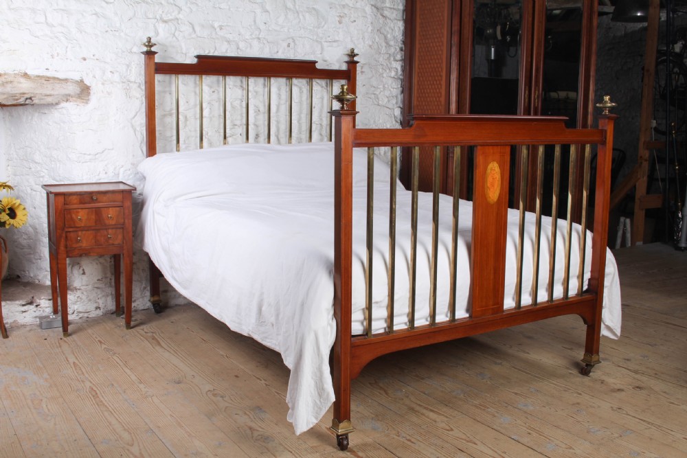 An antique mahogany double bed frame featuring polished brass upright spindles, brass urn finials, and an oval marquetry medallion inlaid on the footboard.