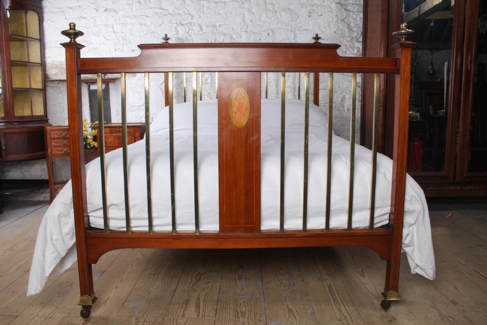 An antique mahogany double bed frame featuring polished brass upright spindles, brass urn finials, and an oval marquetry medallion inlaid on the footboard. View II
