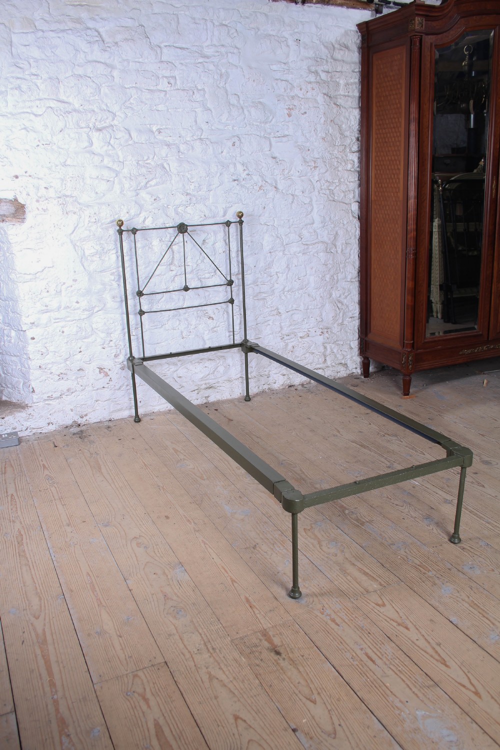 A small Victorian single platform bed constructed from dark green painted iron with brass corner finials. View II
