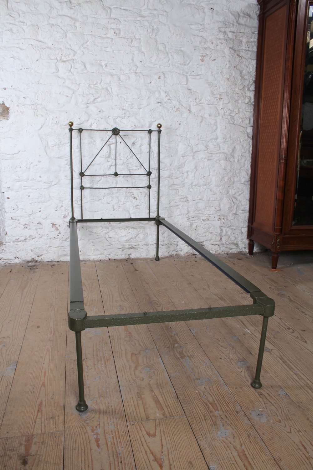 A small Victorian single platform bed constructed from dark green painted iron with brass corner finials. View III