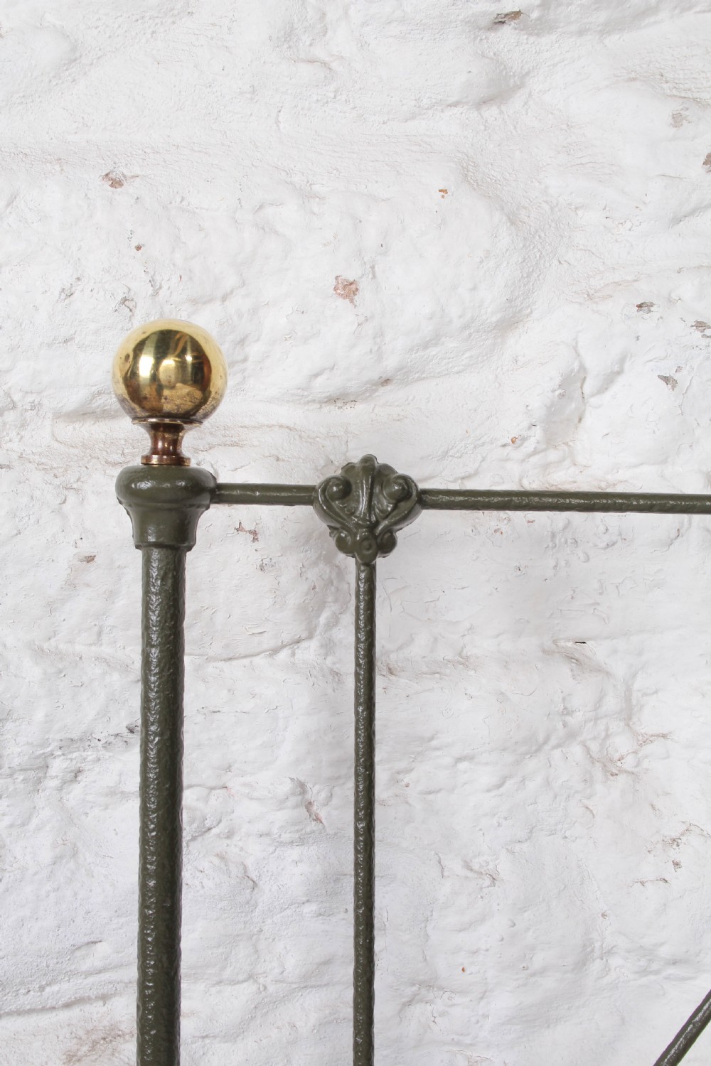 A small Victorian single platform bed constructed from dark green painted iron with brass corner finials. View V