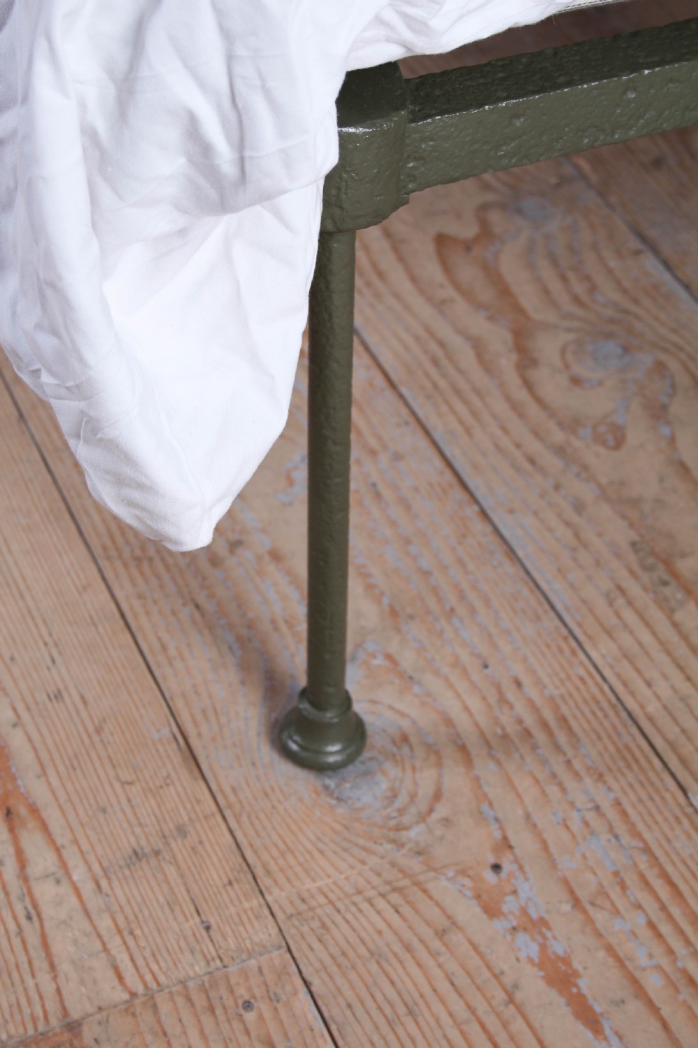 A small Victorian single platform bed constructed from dark green painted iron with brass corner finials. View VII
