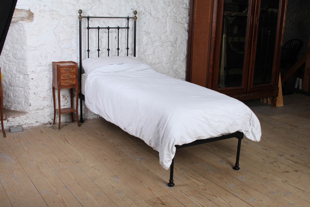 A Victorian single cast iron bedstead with black vertical spindles, brass finials, and white bed linen.