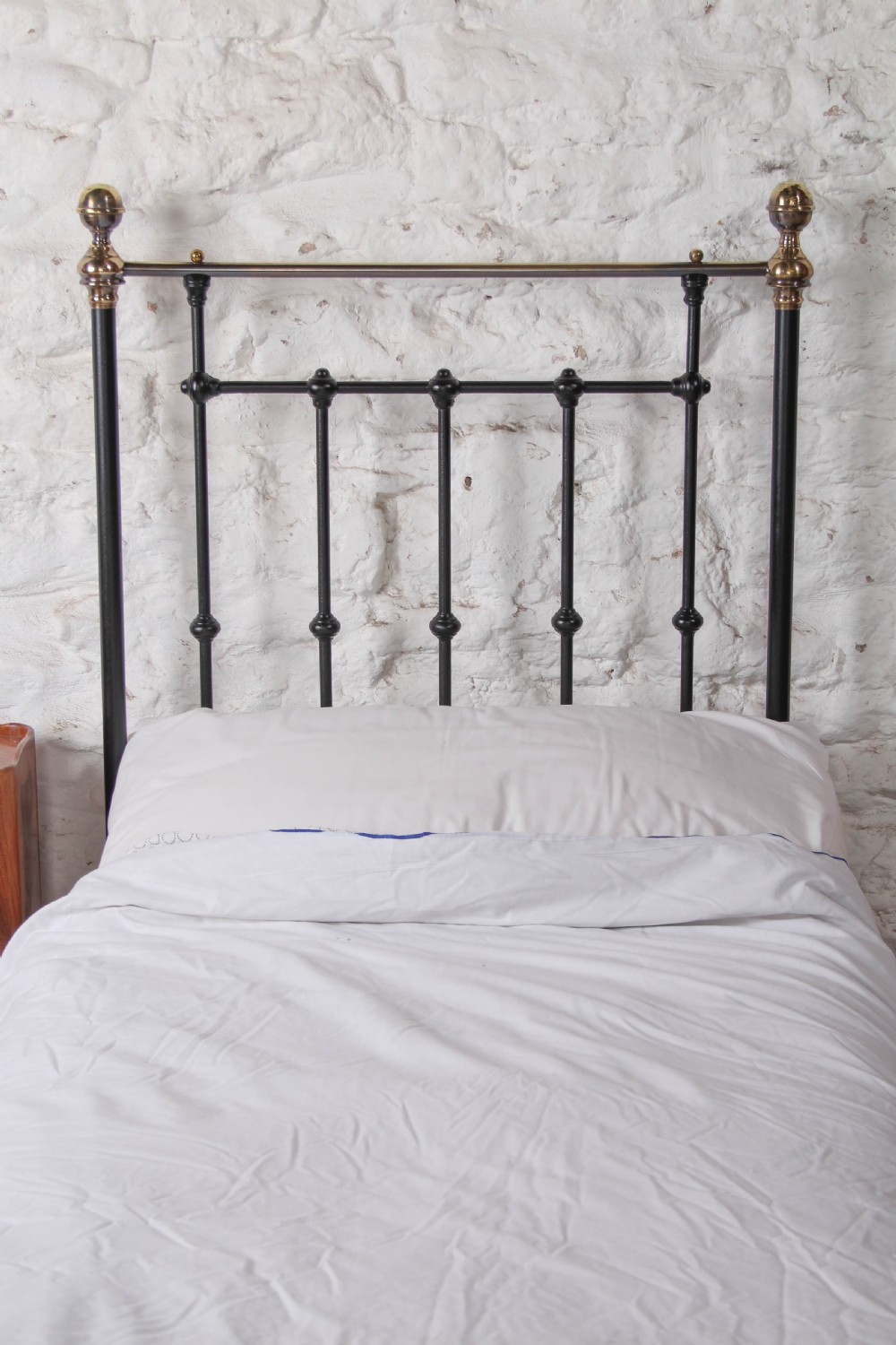 A Victorian single cast iron bedstead with black vertical spindles, brass finials, and white bed linen. View II